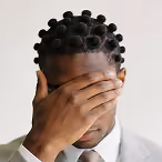 Man with braided hair covering his face with one hand against a plain background.